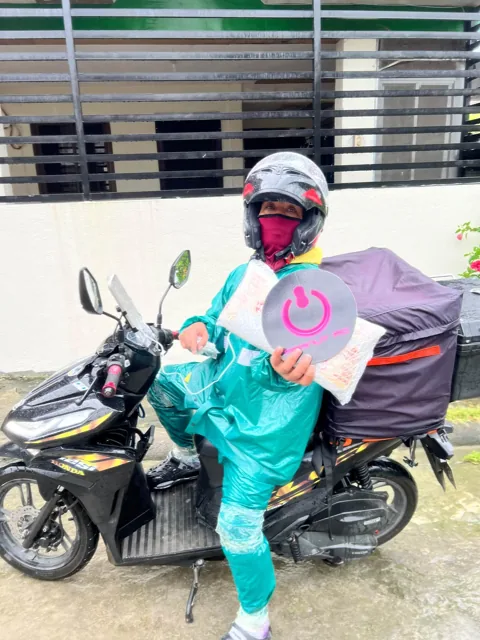 Delivery rider in teal rainwear holding a Peanut PC bag